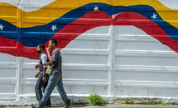 People walk past a mural with the Venezuelan flag.