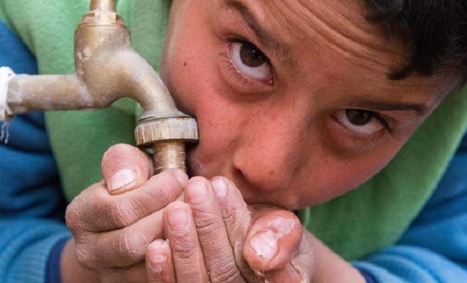 A boy drinks water directly from a tap.