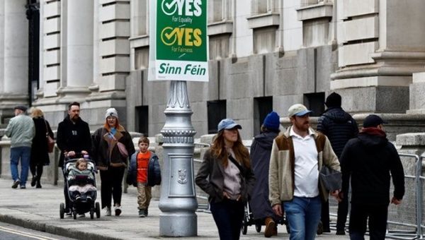 Irish people walk in front of a referedum advertisement, 2024.