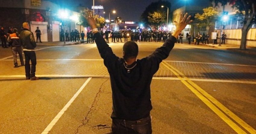 A man kneels in the road in front of a line of police during a demonstration in Los Angeles, California on Nov. 24, 2015 following the grand jury decision in the shooting of Michael Brown. 